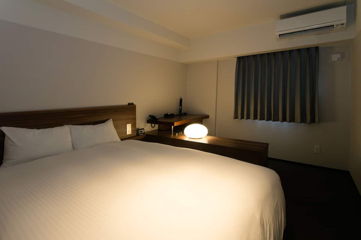 Habitación de hotel con una cama grande, mesita de noche, lámpara y un equipo de aire acondicionado en la pared.