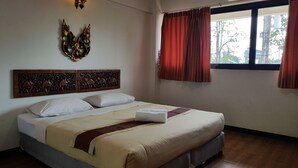 A hotel room with a bed, a decorative headboard, a window with curtains, and an air conditioning unit. - Punya Garden (Phitsanulok)