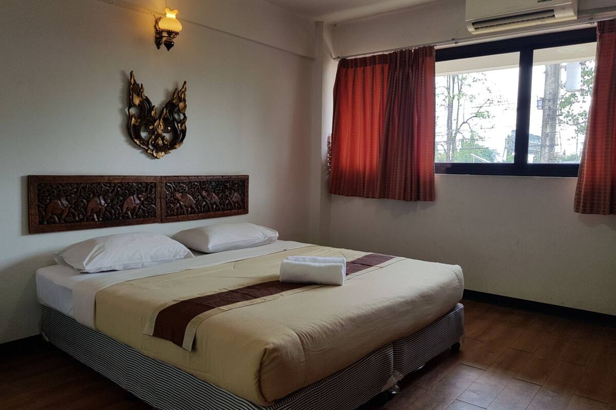 Ein Hotelzimmer mit Bett, einem Zierkopf an der Bettwand, einem Fenster mit Vorhängen und einer Klimaanlage.