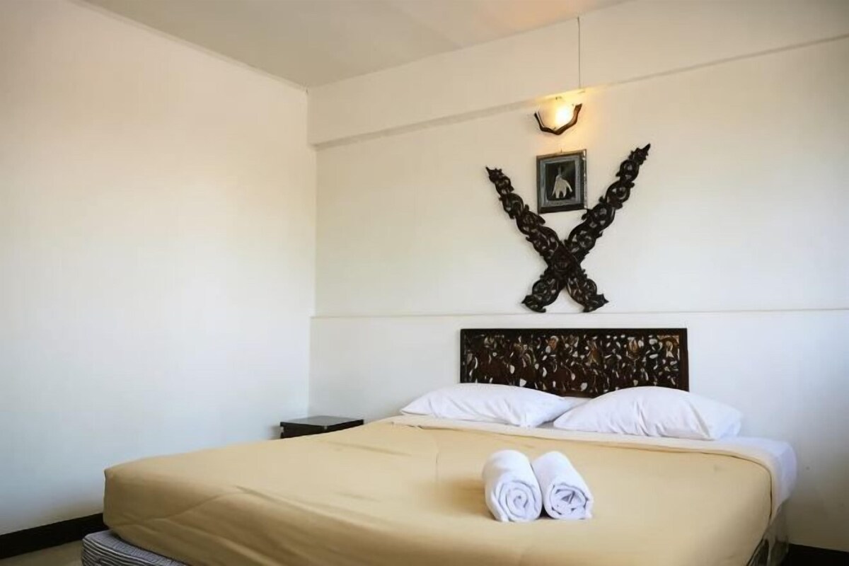 A neatly made bed with a headboard, a wall-mounted light fixture, and a decorative wall piece.