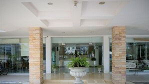 A modern building entrance with glass doors, stone pillars, and a central planter with greenery. - Punya Garden (Phitsanulok)