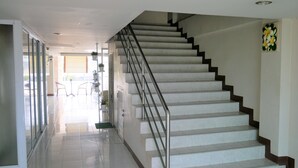 A modern staircase with metal railings, leading to a bright hallway with a glass door and a green mat at the bottom. - Punya Garden (Phitsanulok)