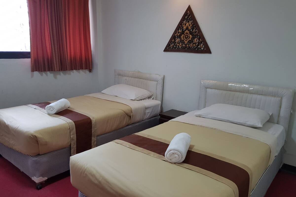 Ein Hotelzimmer mit zwei Betten, jeweils mit beigefarbener und brauner Bettdecke, weißen Kissen und aufgerollten Handtüchern. Darüber befindet sich eine Wanddekoration.