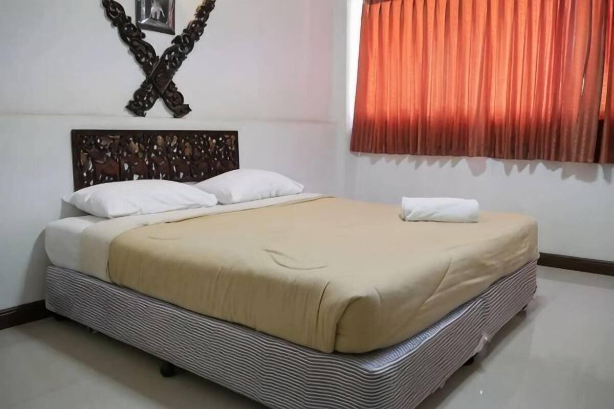Una cama con colchón a rayas, almohadas blancas y una manta color beige.