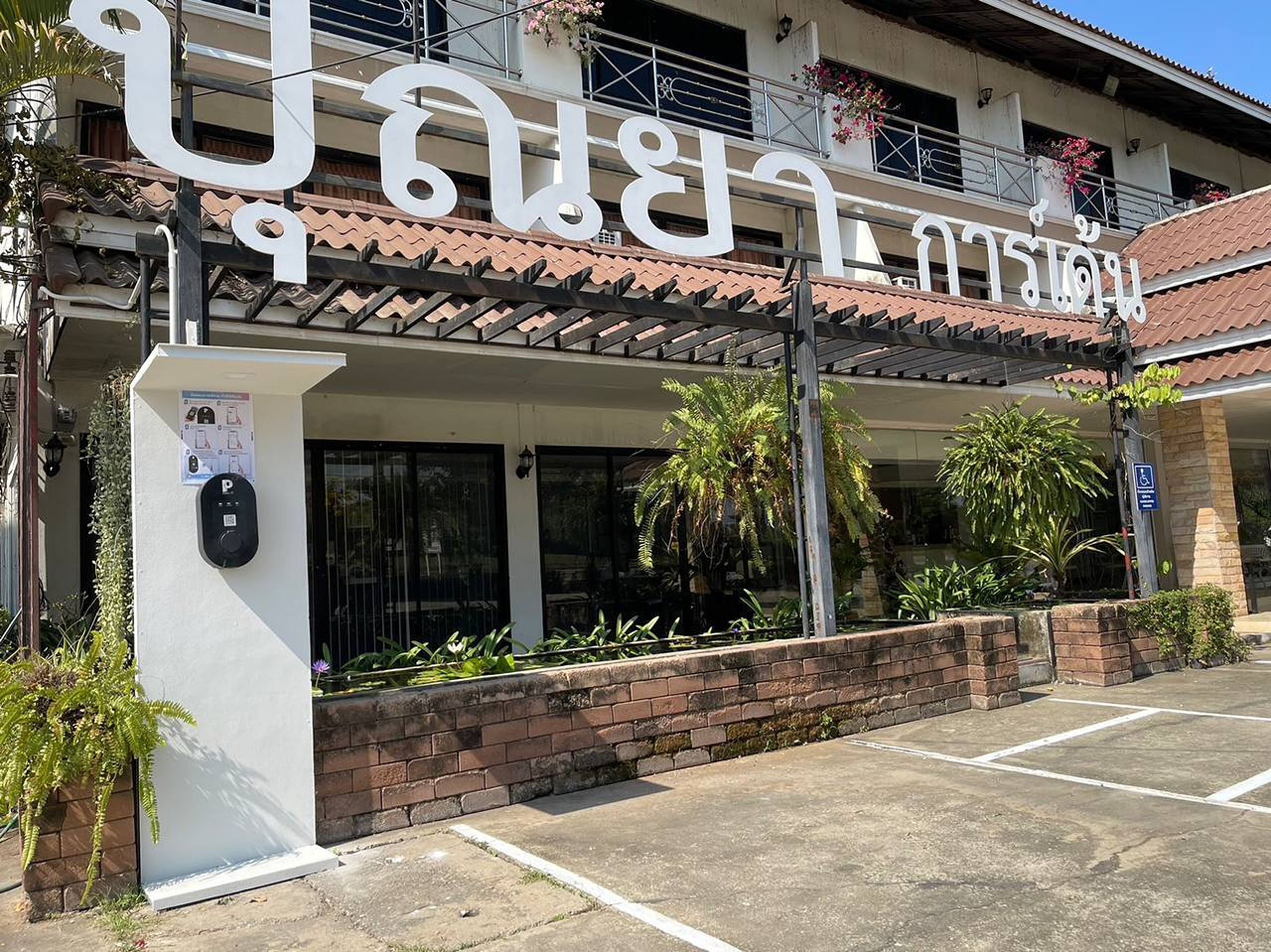 A building with a sign in a foreign script, a covered entrance, and a parking area.