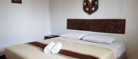 Una cama bien hecha con toallas enrolladas, un adorno en la pared y una mesita de noche con lámpara.