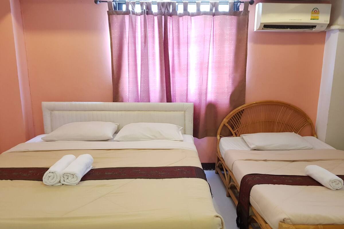 Ein Hotelzimmer mit zwei Betten, einem Korbsessel, einem Fenster mit rosa Vorhängen und einer Klimaanlage.