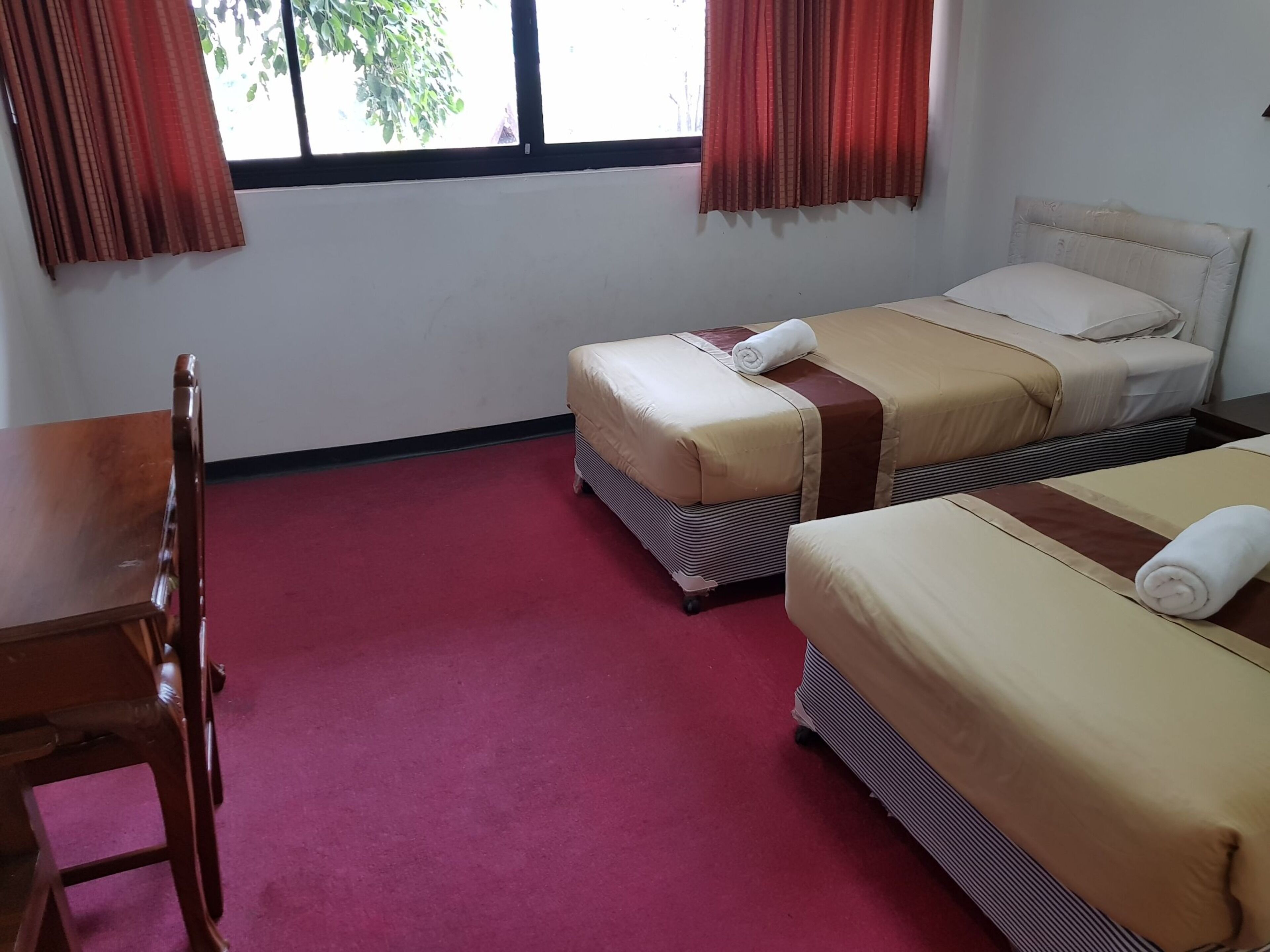 A hotel room with two beds, a desk, and a window with curtains.