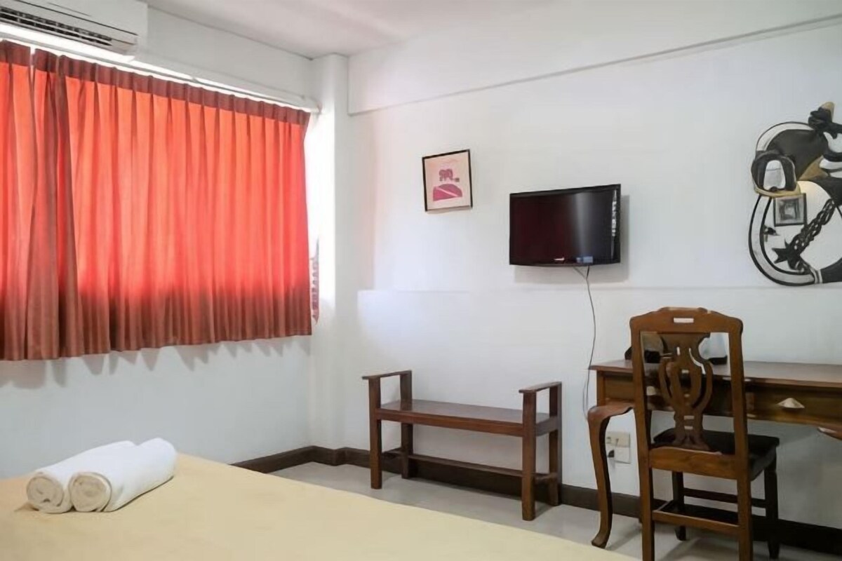 A room with a bed, a desk, a chair, a television, and a window with curtains.