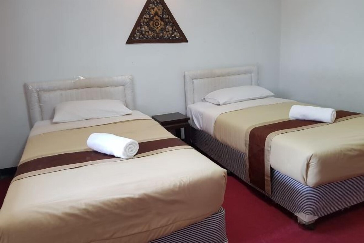 Two single beds with beige and brown bedding, a small nightstand, and a decorative wall piece.