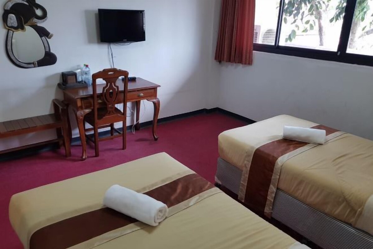 A hotel room with two beds, a desk with a chair, a television, and a window with curtains.