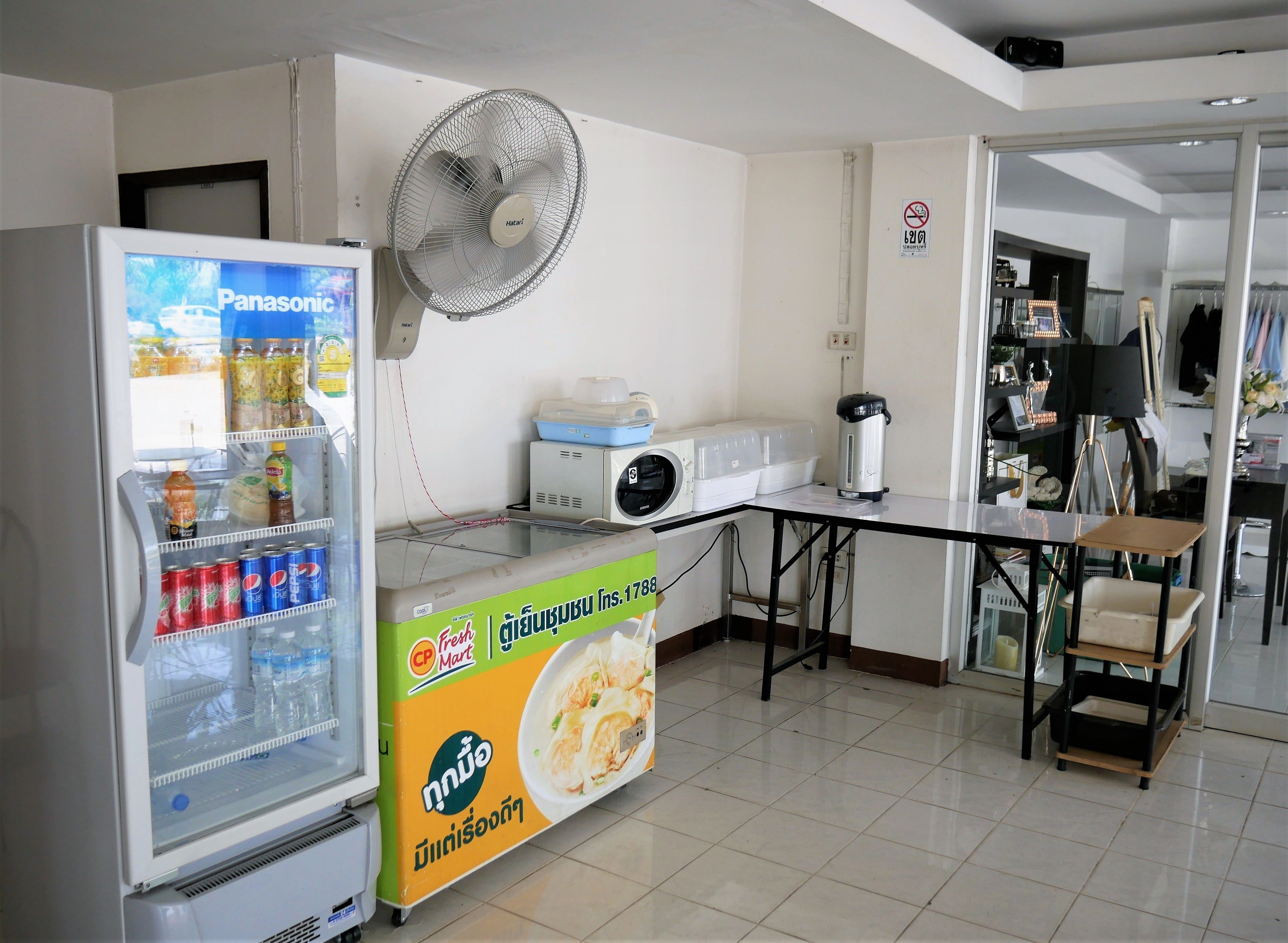 A kitchenette with a refrigerator stocked with beverages, a microwave, a coffee maker, and a fan.