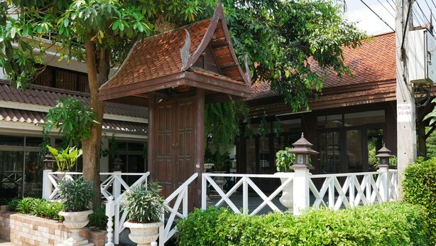 A traditional wooden structure with a tiled roof, surrounded by a white fence and potted plants. - Punya Garden (Phitsanulok)