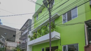 Un edificio de varios pisos con fachada verde, balcones con plantas y un coche visible en primer plano.