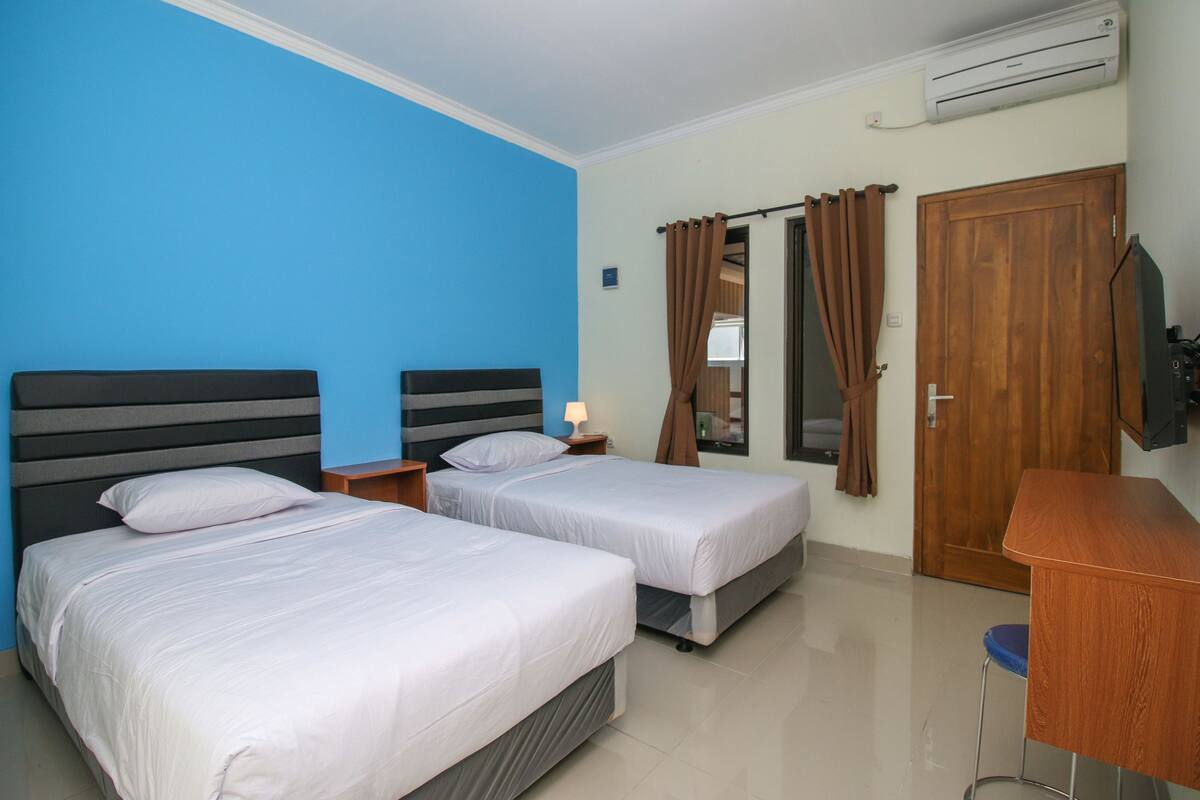A hotel room with two beds, a desk, a chair, an air conditioner, and a wooden door.