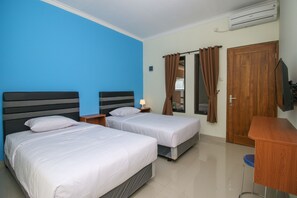 A hotel room with two beds, a desk, a chair, an air conditioner, and a wooden door. - Sky Residence Syariah Mampang 1 Jakarta (Jakarta)