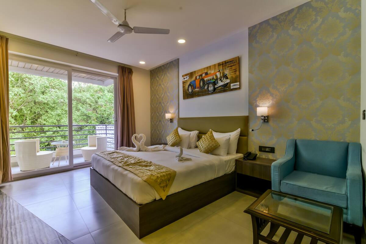 Quarto de hotel com uma cama grande, um sofá, mesa de centro de vidro e varanda com área de estar externa.