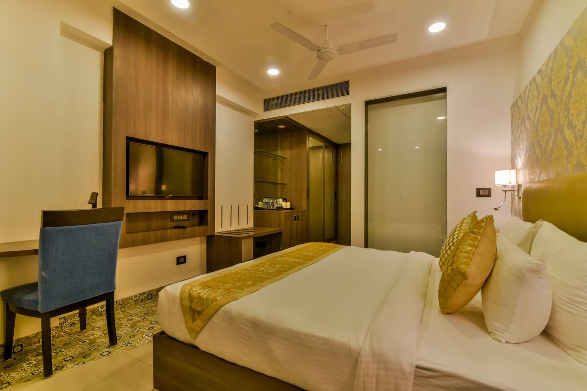 Quarto de hotel com uma cama, uma escrivaninha com cadeira, televisão e ventoinha no teto.