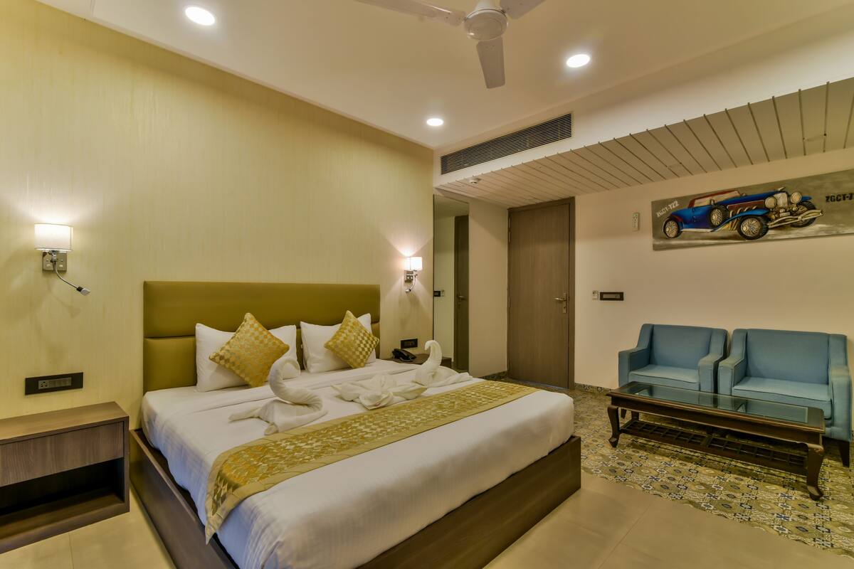 Quarto de hotel com cama, escrivaninha, cadeira, ventoinha no teto e uma obra de arte na parede.