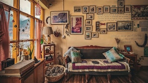 Una habitación acogedora con un sofá de madera, un ventanal con cortinas y una pared decorada con cuadros y citas.