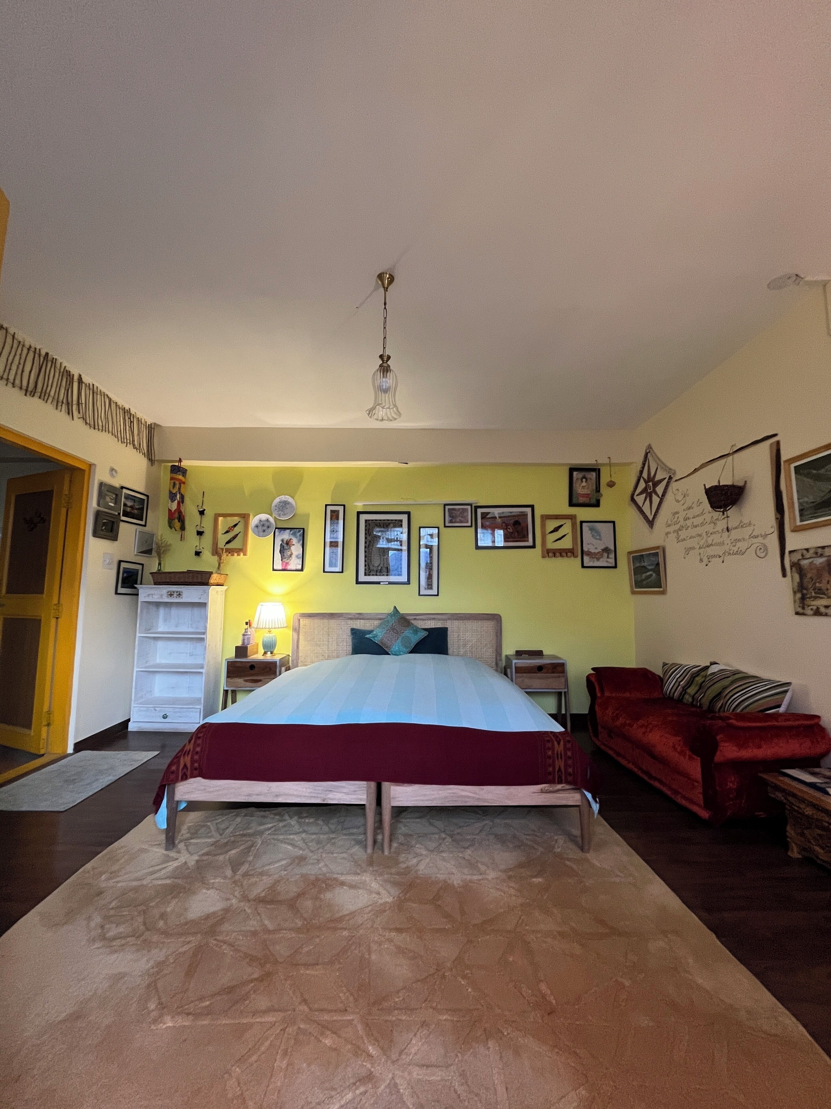 A bedroom with a bed, a red sofa, a nightstand, and a wall decorated with pictures.