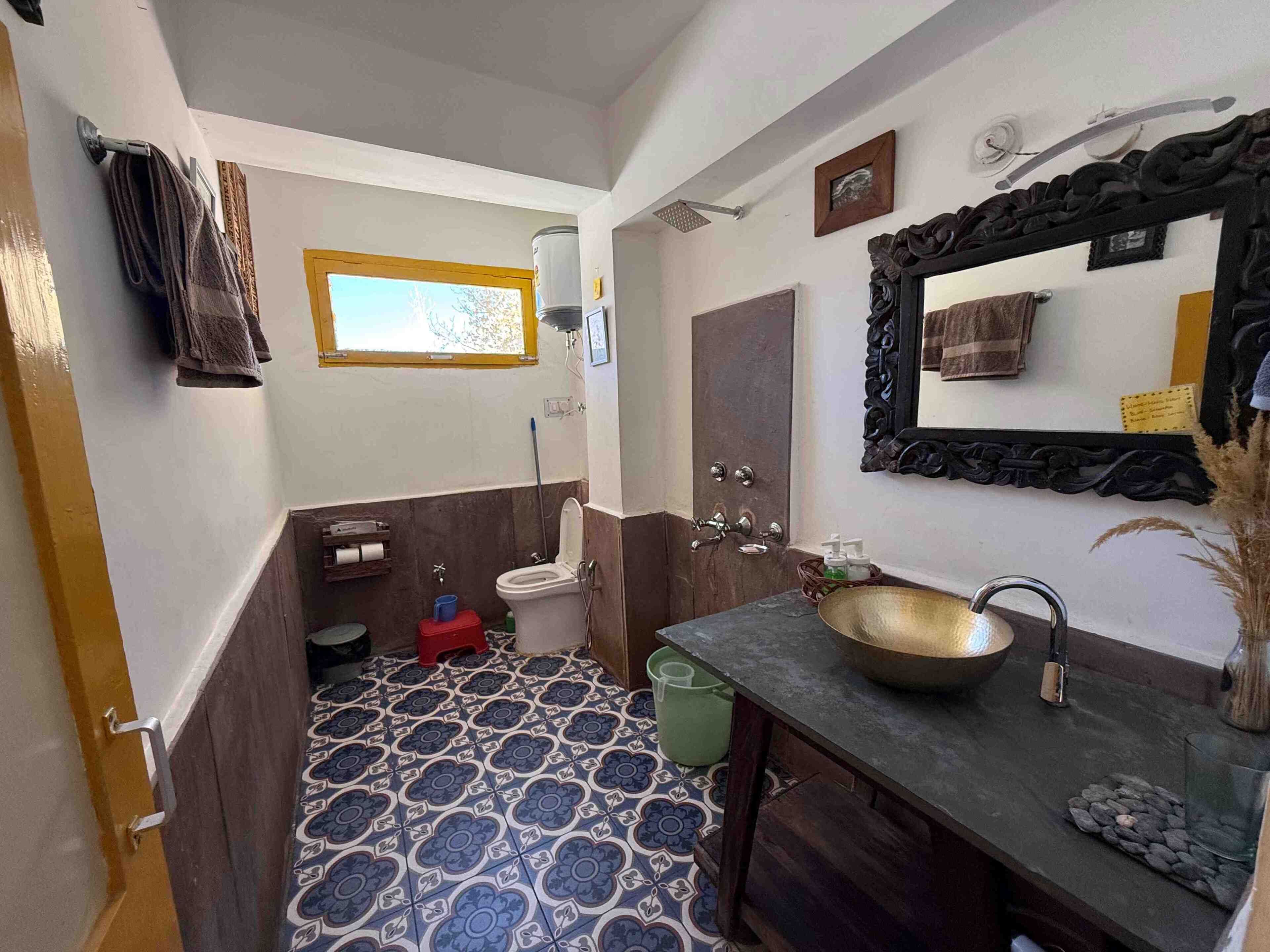 Une salle de bain équipée de toilettes, d’un lavabo et d’une douche. Il y a une fenêtre au-dessus des toilettes et un miroir au-dessus du lavabo.