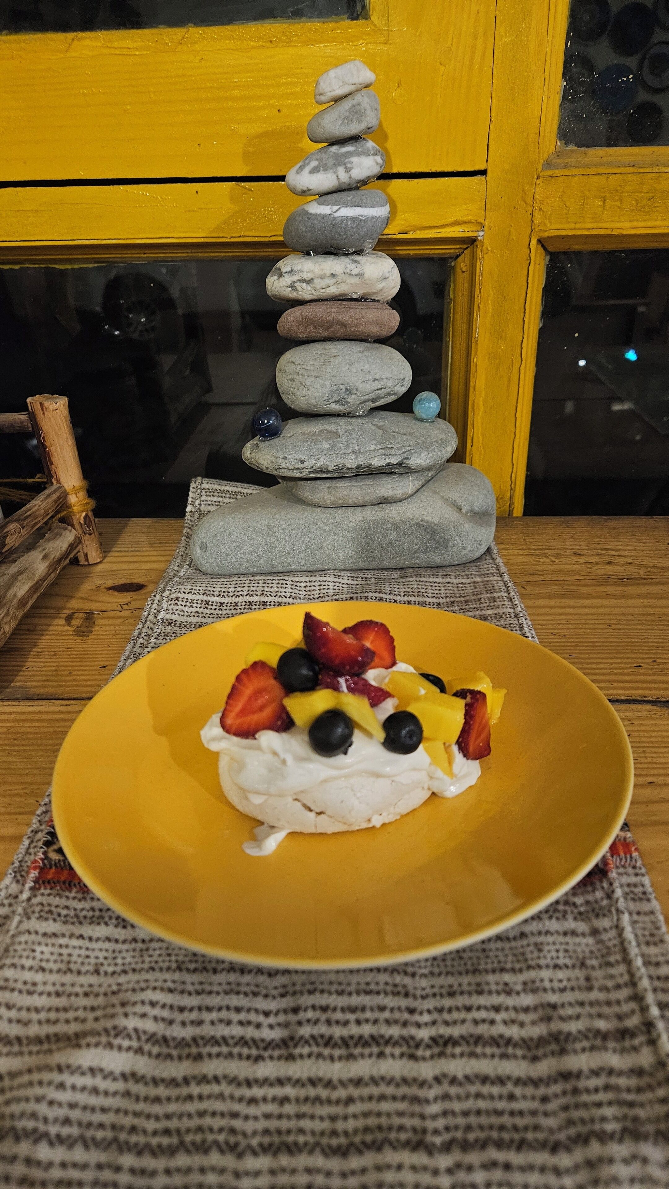 A yellow plate with a dessert topped with strawberries, blueberries, and mango slices, placed on a woven placemat.