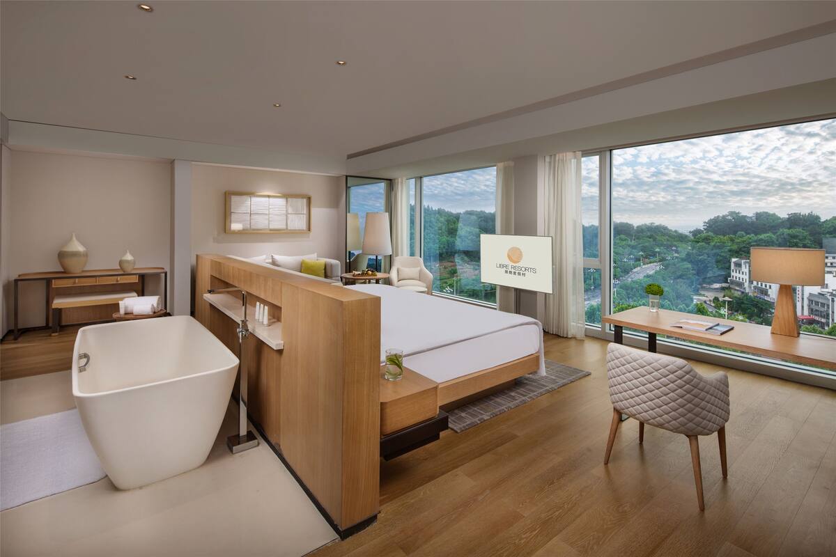 Une chambre d’hôtel moderne dotée d’un grand lit, d’une baignoire, d’un coin salon avec vue et d’un bureau avec un ordinateur portable.