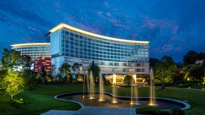 A modern hotel with a curved glass facade, a central courtyard with fountains, and well-maintained greenery. - Libre Resorts Huangshan (Huangshan)