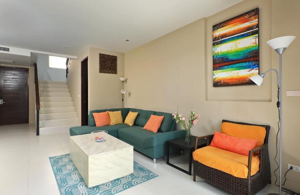 A modern living room with a green sofa, a white coffee table, a wicker chair, and a colorful abstract painting on the wall.