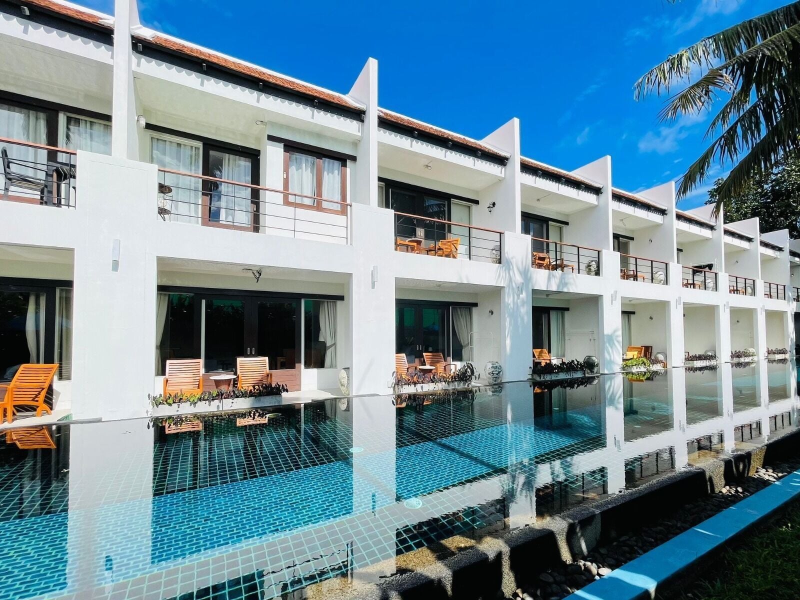 Un hôtel à plusieurs étages doté d’une piscine à débordement dont le fond est en verre, d’un espace extérieur aménagé et offrant une vue sur un ciel d’un bleu éclatant.