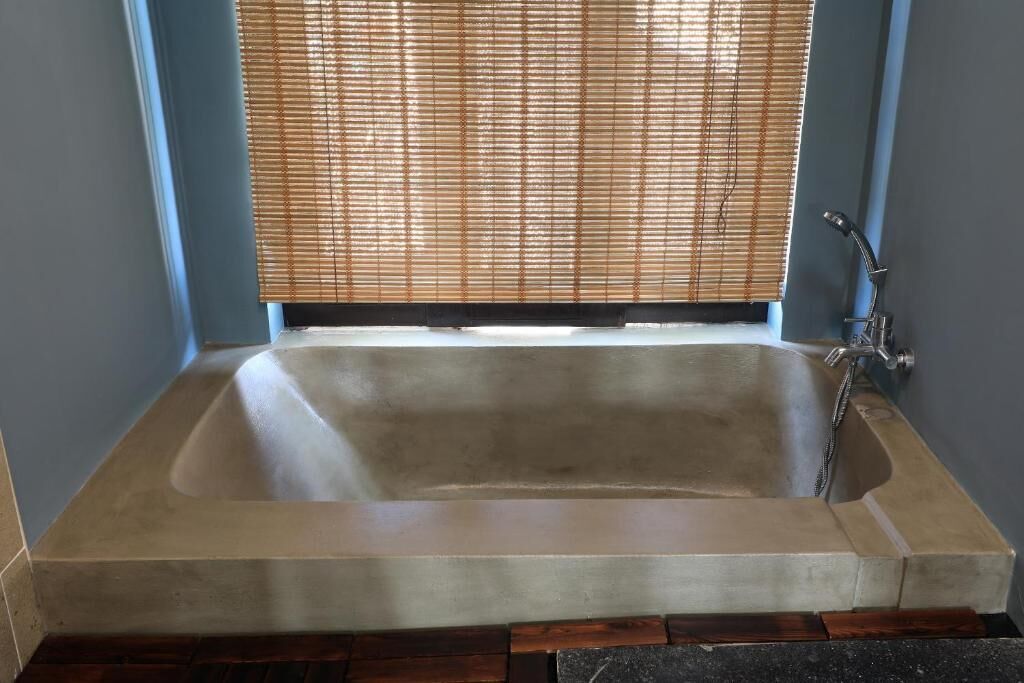 A rectangular bathtub with a showerhead, set against a wall with a window covered by blinds.