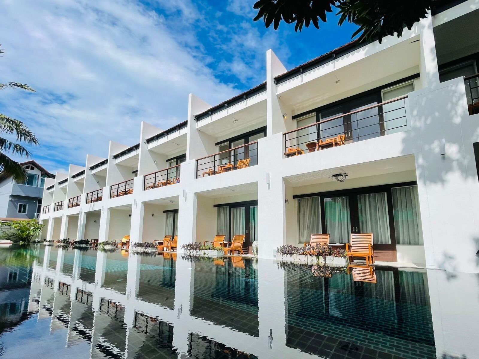 A modern hotel with multiple balconies, a swimming pool, and outdoor seating areas.