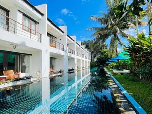 A modern hotel with a swimming pool, outdoor seating, and lush tropical vegetation. - Tea Tree Boutique Resort (Rawai)