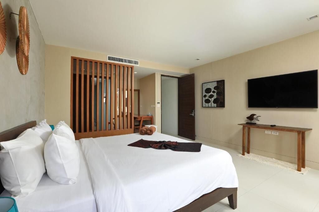 A hotel room with a bed, a wooden partition, a television, and a small table.