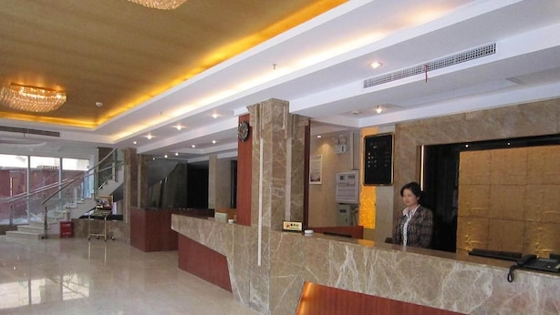 Zona de recepción de un hotel, con un mostrador de mármol, un reloj y una escalera al fondo.