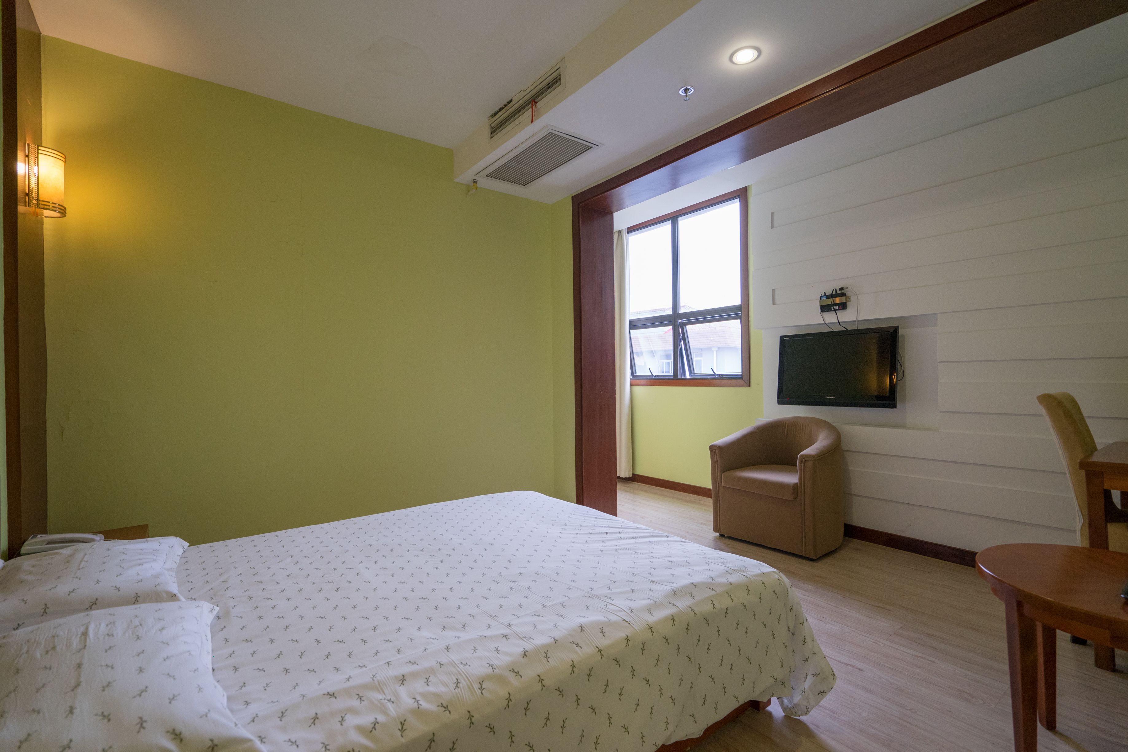 Una habitación de hotel con una cama, televisión en la pared, una ventana y una silla.