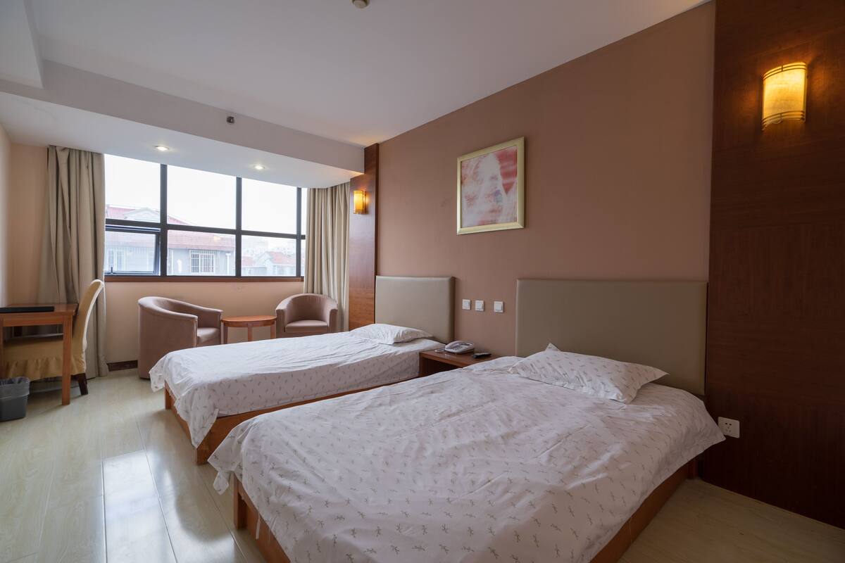 Habitación de hotel con dos camas, un escritorio, una silla y una ventana con cortinas.