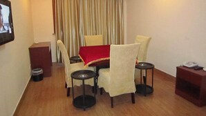 Habitación de hotel con una mesa de comedor, cuatro sillas, mantel rojo, una mesita redonda pequeña, teléfono y un cubo de basura.