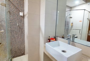 A bathroom with a glass shower enclosure, a white sink, and a mirror.