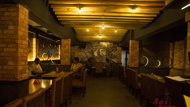 A restaurant interior with brick walls, wooden tables, and a mural on the back wall. - Hotel Prem Nivas (Madurai)