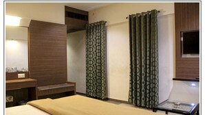 A hotel room with a bed, a small table, a mirror, a wooden cabinet, and patterned curtains. - Hotel Prem Nivas (Madurai)
