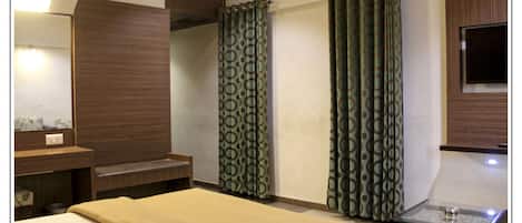 A hotel room with a bed, a small table, a mirror, a wooden cabinet, and patterned curtains.