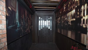 A corridor with a dark wooden door, brick walls, and a tiled floor. - Hotel Prem Nivas (Madurai)