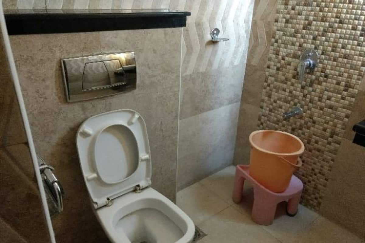 A bathroom with a toilet, a bidet, and a small pink stool with a bucket.