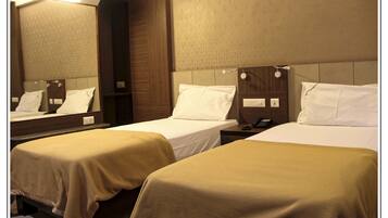 Habitación de hotel con dos camas individuales, cada una con cabecero de madera y almohada blanca.