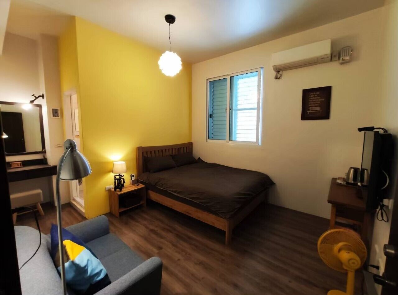 Un dormitorio con cama, mesitas de noche, lámpara, ventilador y ventana con persianas.