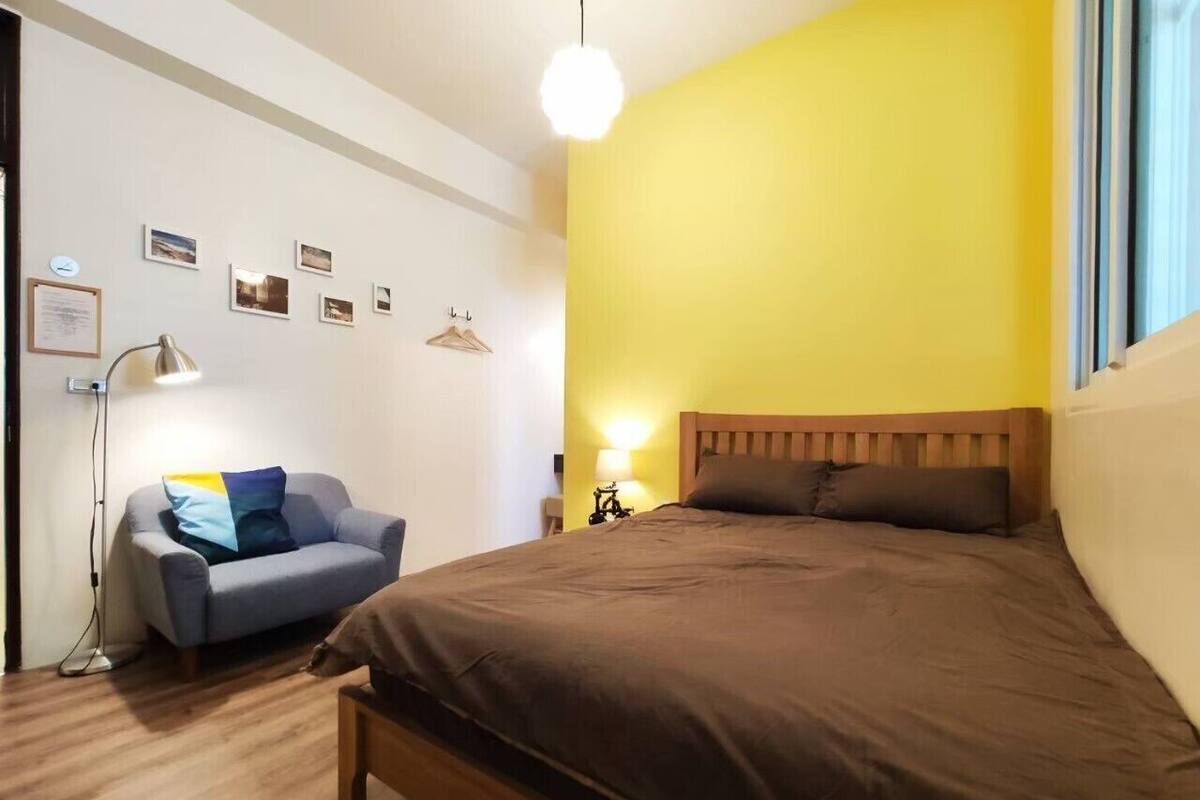 A bedroom with a bed, a sofa, a bedside table, a lamp, and a window.