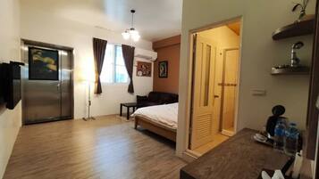 A compact hotel room with a bed, a desk, a chair, a small table, a wardrobe, a door, and a window with curtains.