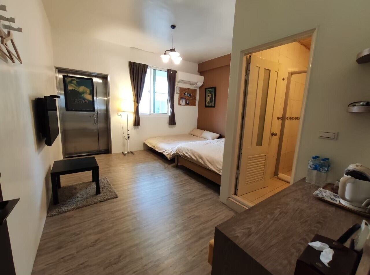 A compact hotel room with a bed, a small table, a refrigerator, and a kitchenette area.